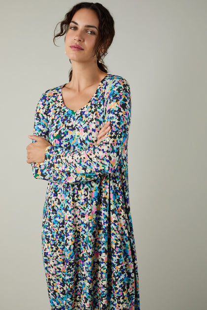 A woman with arms crossed wears the Colourful Confetti Jersey Bubble Dress, showcasing its abstract confetti print and cocoon silhouette, set against a plain light gray background.