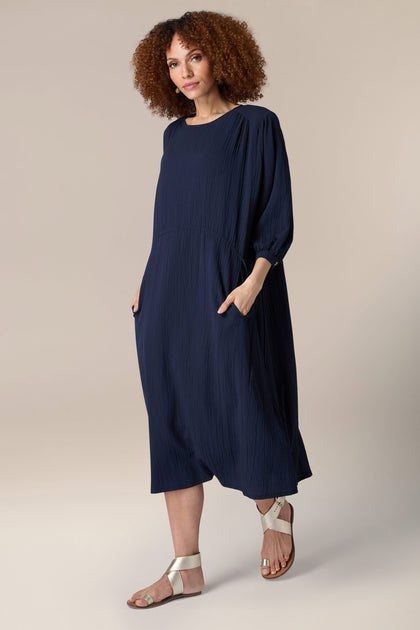 The model is wearing a relaxed fit Crinkle Soft Viscose Flared Dress with pockets and sandals.