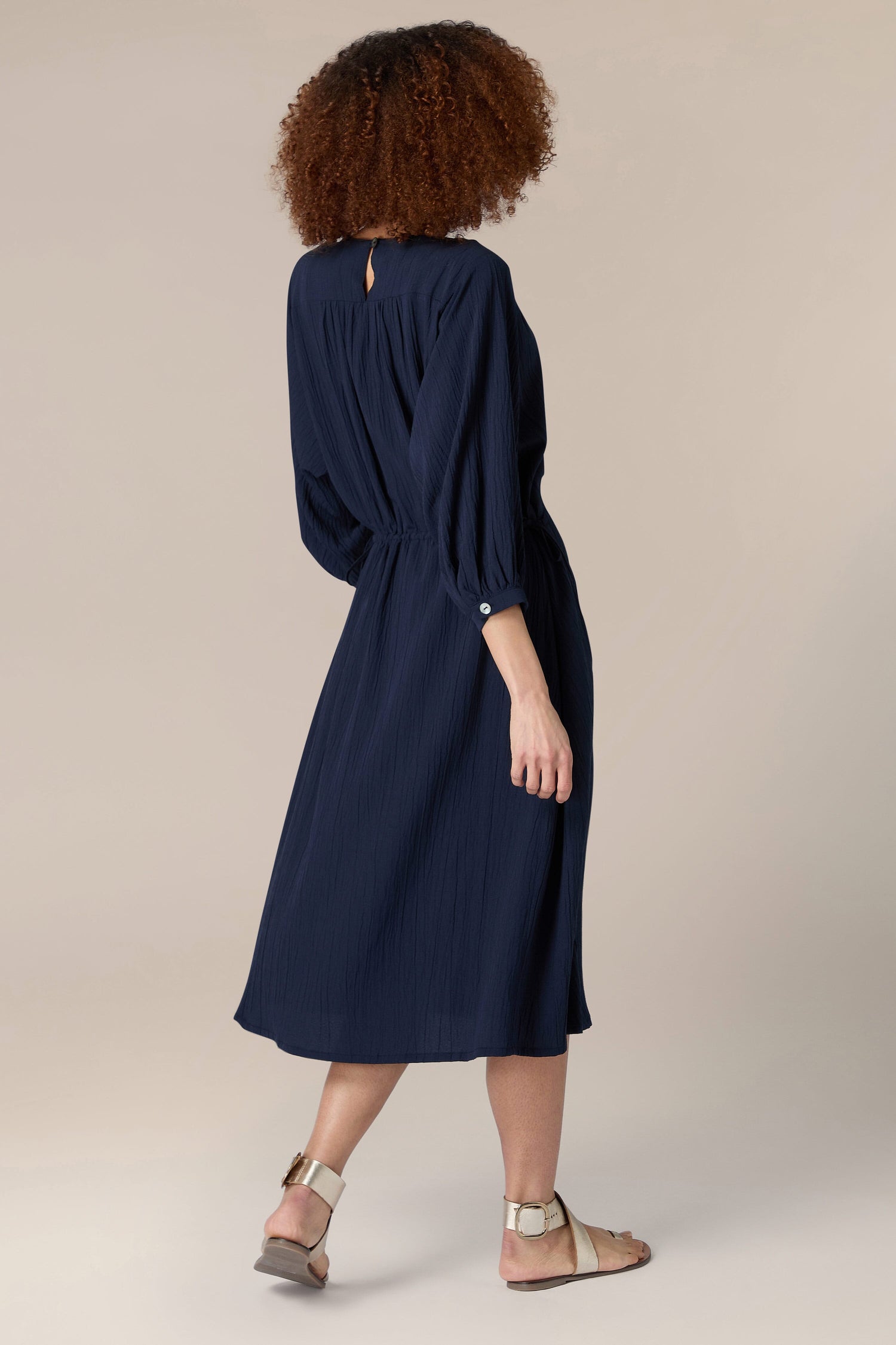 The back view of a woman wearing a navy midi Crinkle Soft Viscose Flared Dress with a scoop neck design.