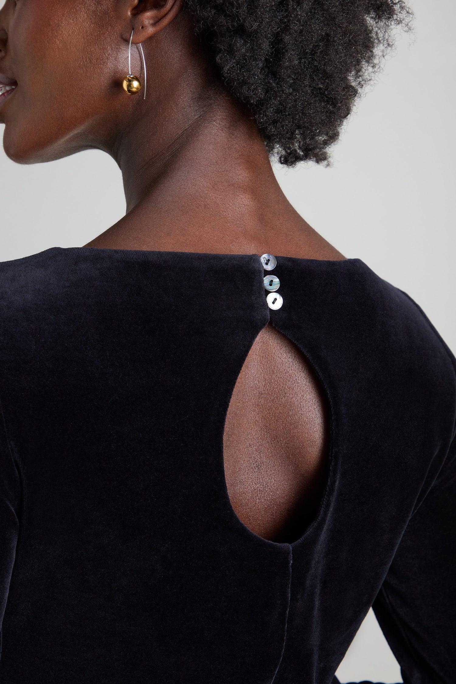 Close-up of the back of a person exuding subtle elegance, donned in a black Velvet Jersey Maxi A-Line Dress featuring a teardrop cutout and three buttons at the neckline.