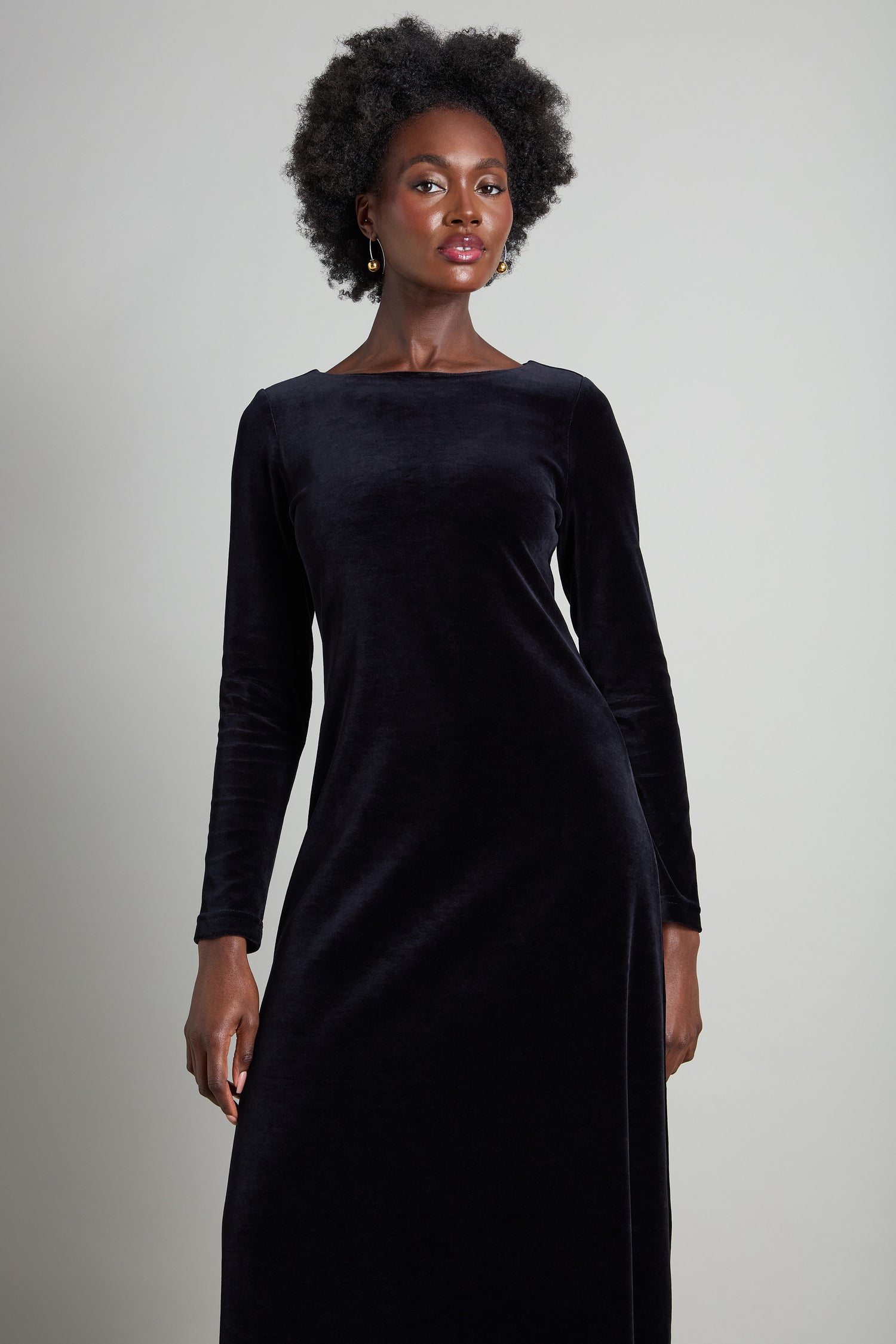 A person in a sophisticated Velvet Jersey Maxi A-Line Dress, showcasing a fit-and-flare silhouette, stands against a plain background, exuding understated glamour.