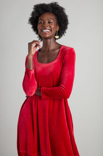 A person wearing the Velvet Jersey Bubble Dress, crafted from plush, stretchy velvet fabric with a distinctive horseshoe neckline, smiles with their eyes closed while standing against a plain background.