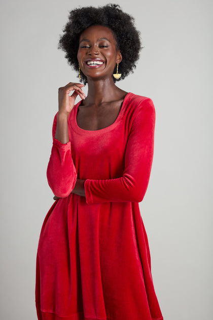 A person wearing the Velvet Jersey Bubble Dress, crafted from plush, stretchy velvet fabric with a distinctive horseshoe neckline, smiles with their eyes closed while standing against a plain background.