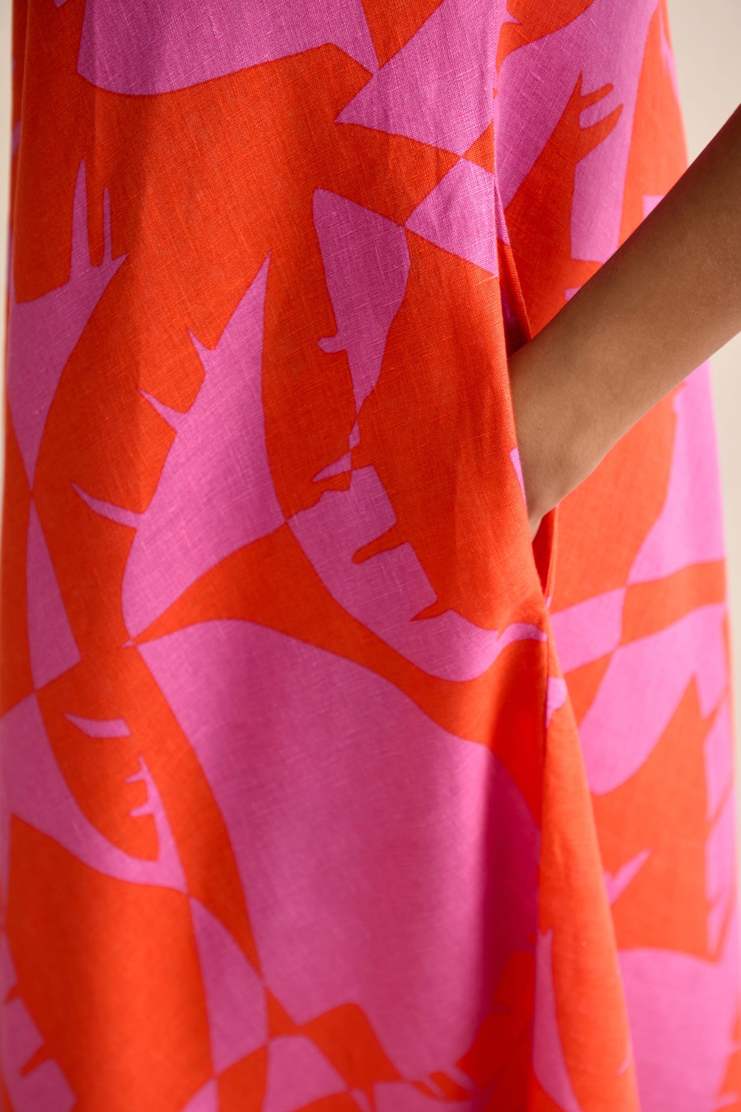 A close-up of the Palm Mirage Linen Flared Dress, featuring an abstract red and pink pattern and a side pocket where a person’s hand rests.