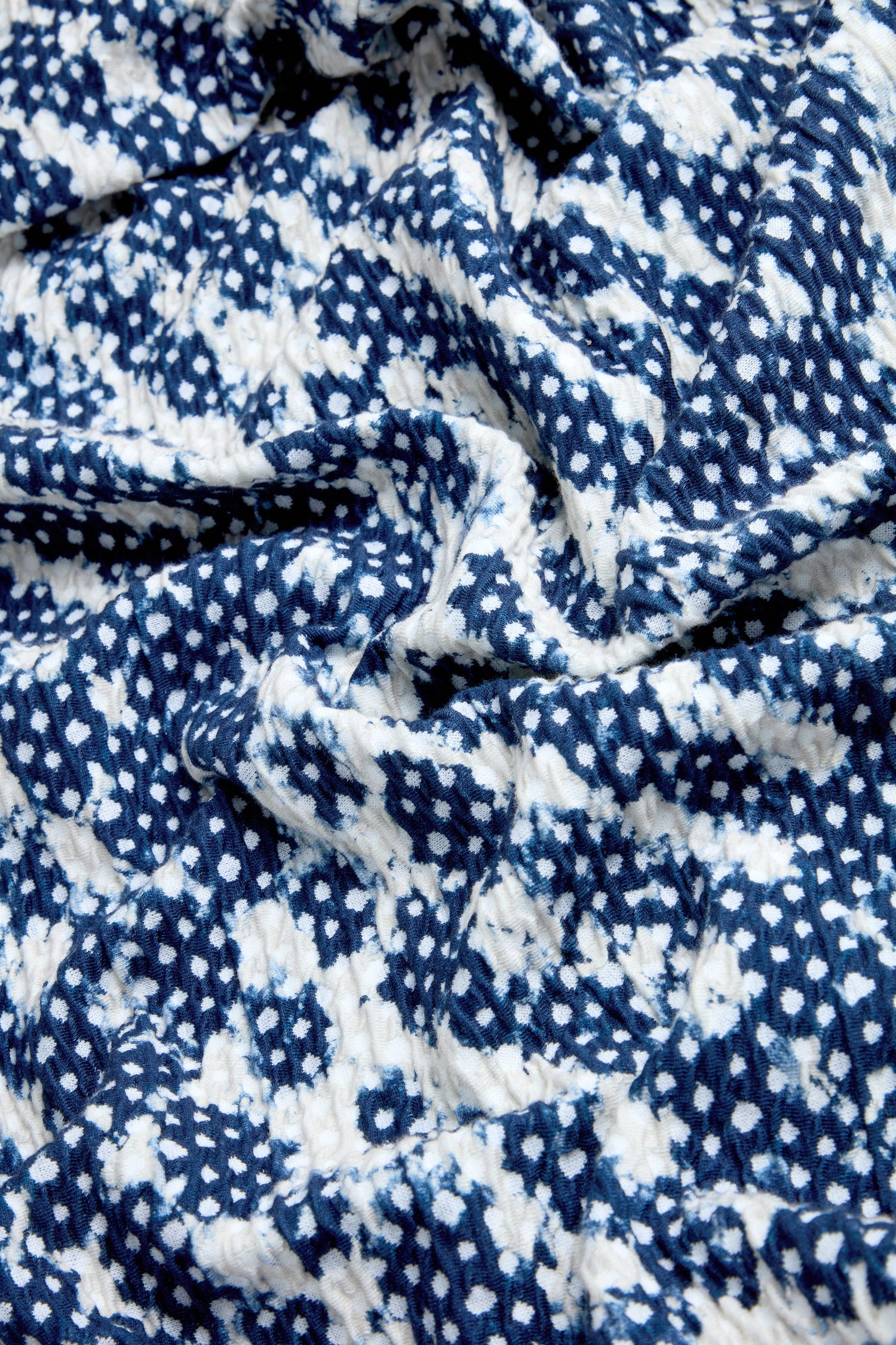 A close-up of crumpled fabric with a blue and white geometric pattern from the Diamond Tie Dye Jersey Jacket, made in England.