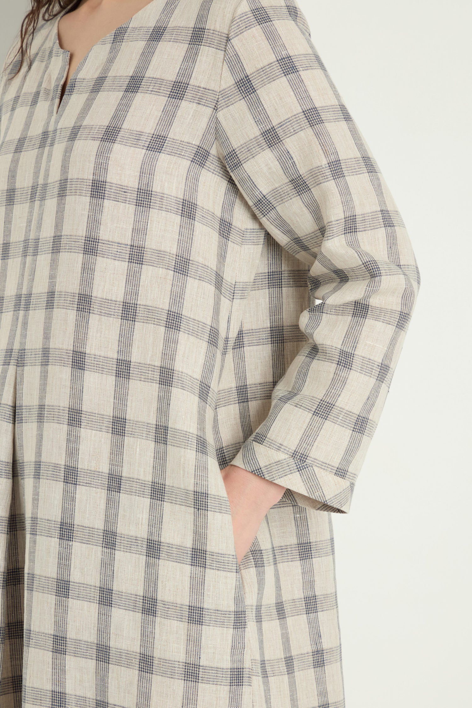 Wearing the Grid Check Linen Dress in beige linen with a navy grid pattern and three-quarter sleeves, one hand placed in a side pocket.