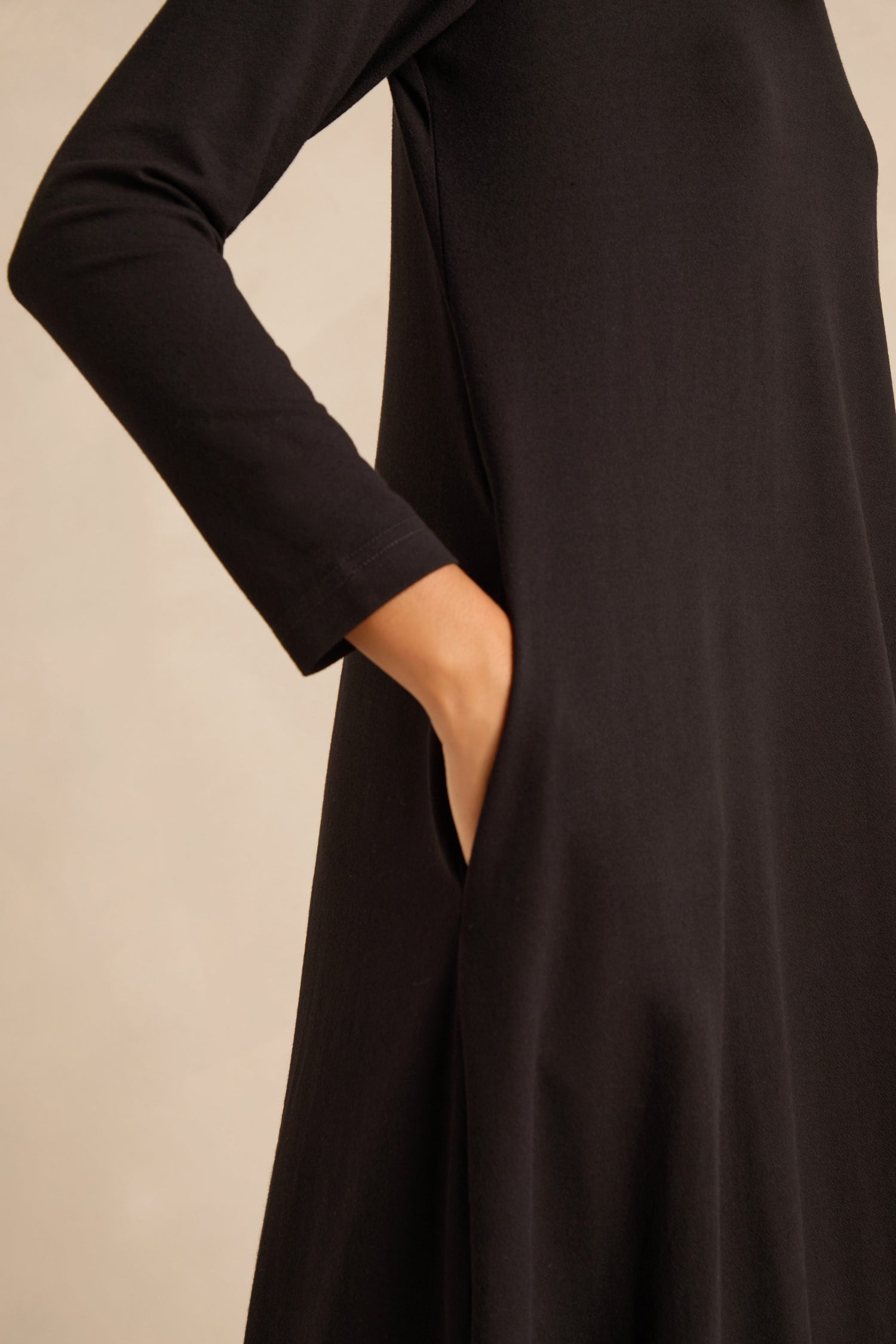 Person wearing the Fluid Crepe Bubble Dress in black, featuring long sleeves and one hand placed in the side pocket, shown from the neck to mid-thigh.