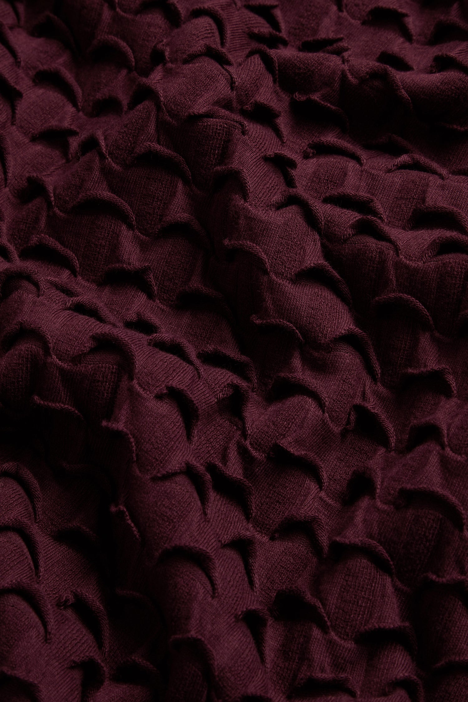 Close-up of the Origami Pocket Jersey Cowl Neck Dress in dark burgundy, featuring textured jersey fabric with a raised geometric pattern and scalloped shapes throughout the surface.