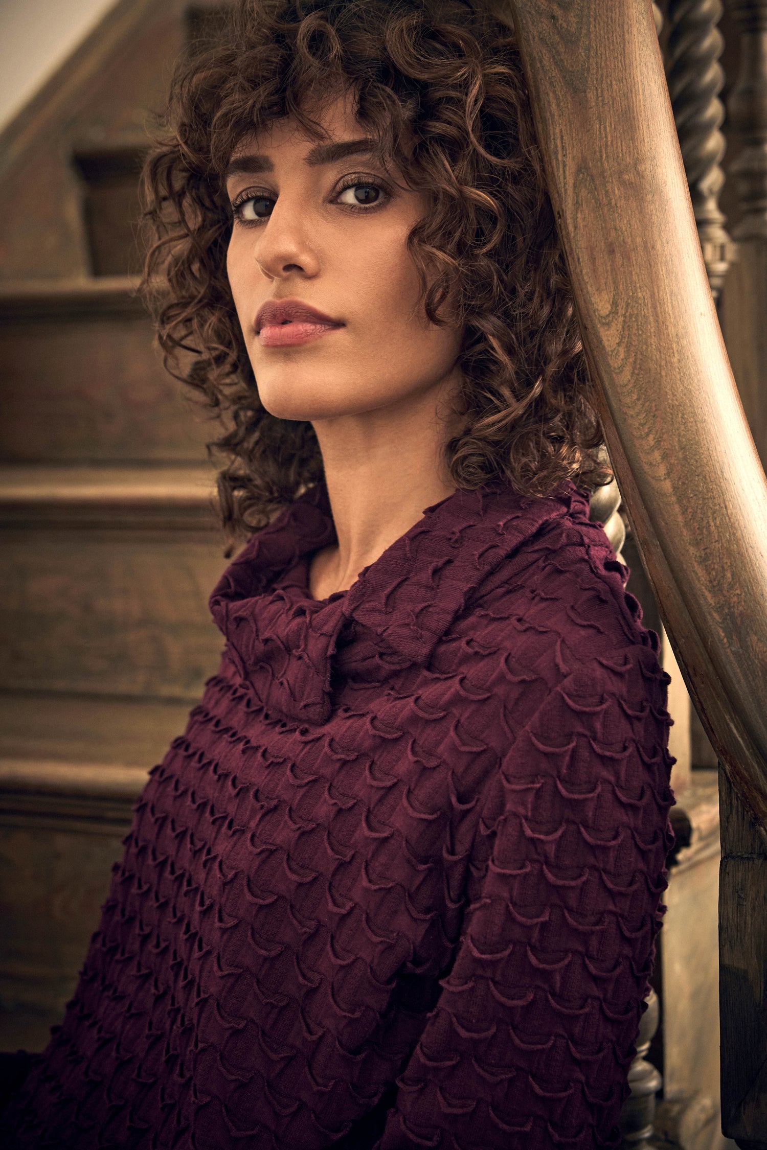 A person with curly hair wearing a deep purple, textured, scaled-pattern Origami Pocket Jersey Cowl Neck Dress.