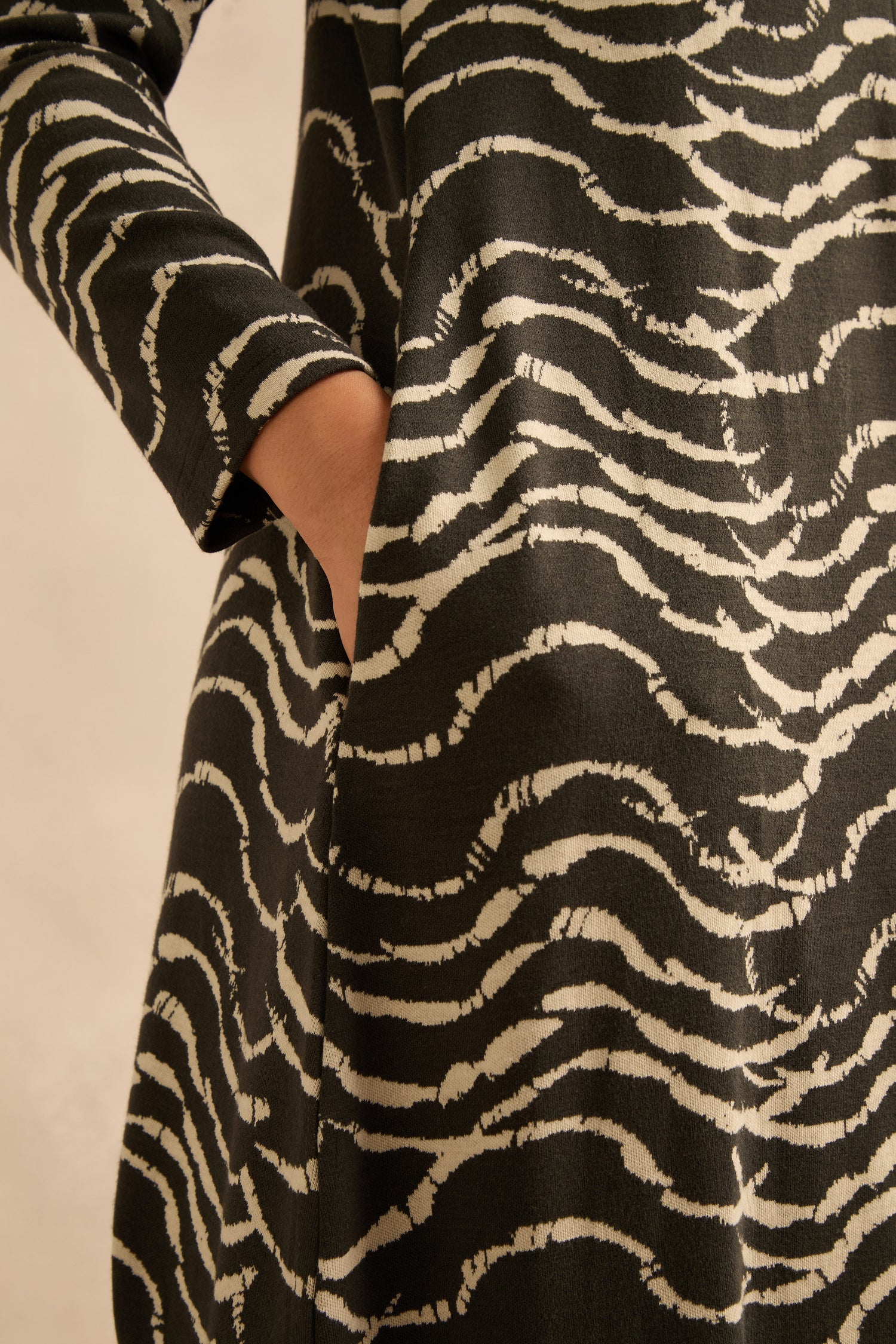 Close-up of a person’s hand in the pocket of the Dancing Waves Jersey Zip Neck Dress, featuring a black and white animal print and long sleeves, shown from chest to mid-thigh. The bubble silhouette adds a modern twist to this comfortable stretch jersey piece.