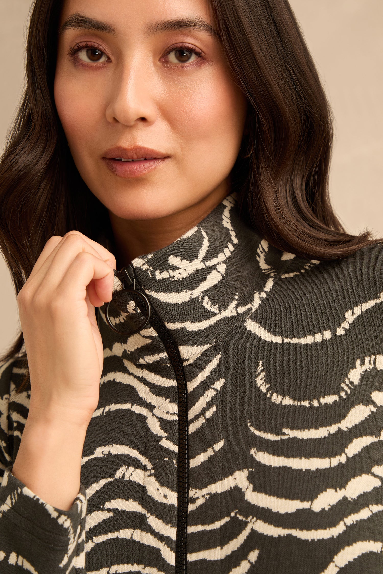A woman with long dark hair wears the Dancing Waves Jersey Zip Neck Dress, holding the zipper near her chin and looking at the camera.