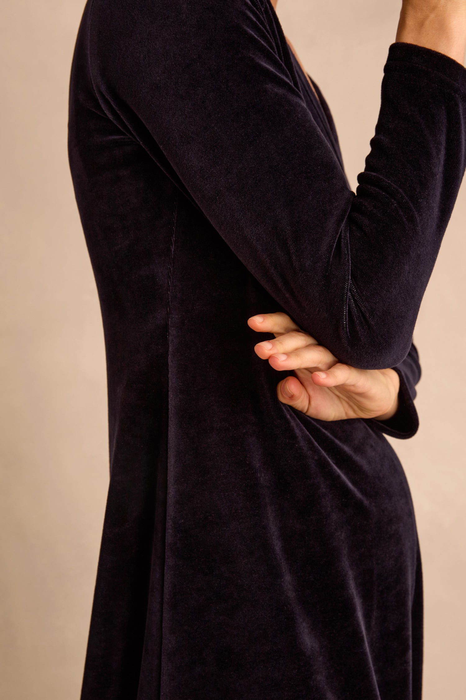 A person wearing the Night Velvet Jersey Maxi Dress—a long-sleeved, cotton-rich velvet piece—stands with arms crossed, photographed in profile against a neutral background; the fit-and-flare silhouette subtly enhances its elegant look.