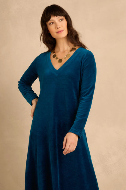 A woman wearing a Teal Velvet Jersey Maxi Dress in a teal V-neck long-sleeve fit-and-flare silhouette with a gold disc necklace.