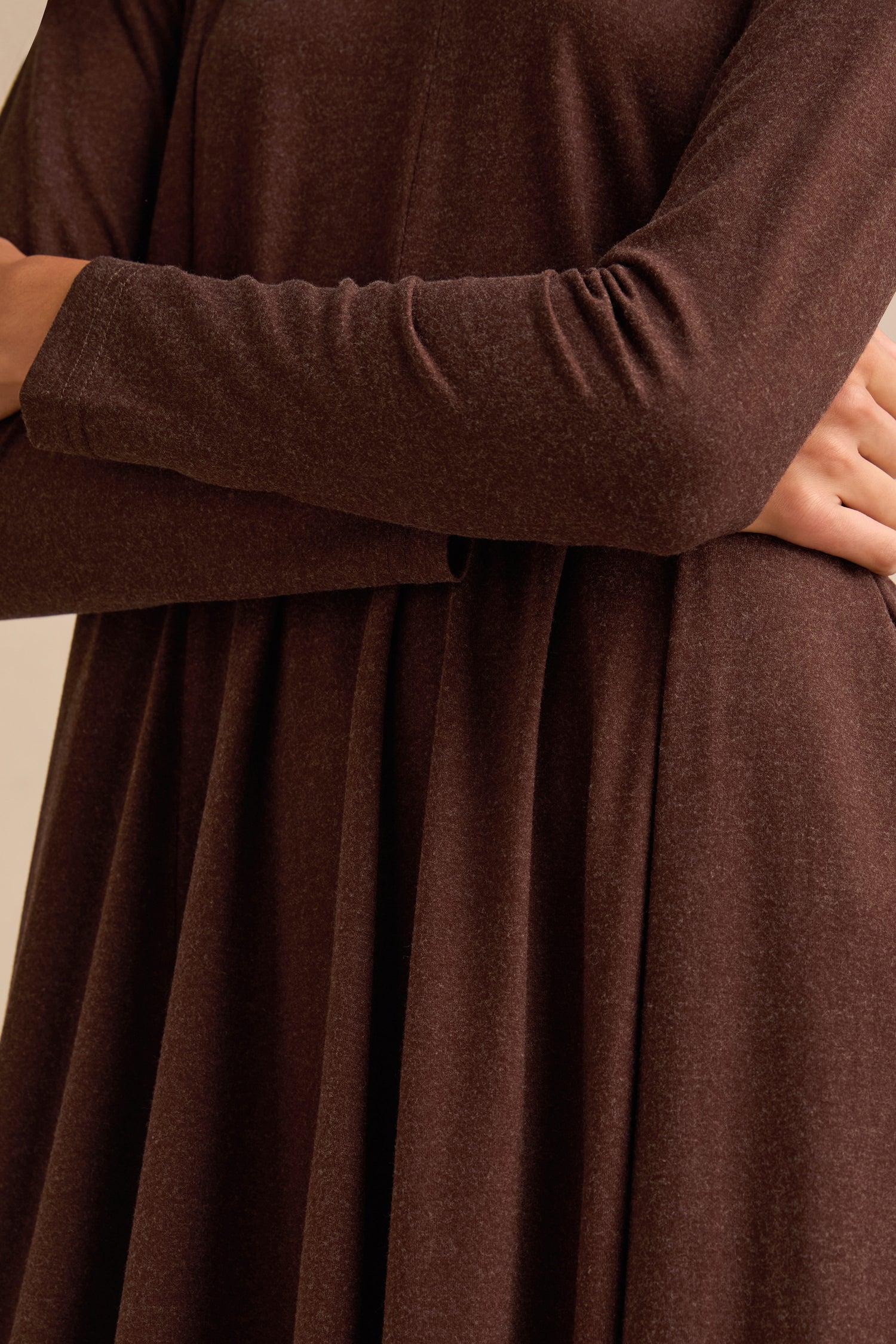 Wearing the Soft Viscose Jersey Bubble Dress, this person is shown from shoulders to waist with arms crossed; the dress features long sleeves and a brown midi bubble silhouette.