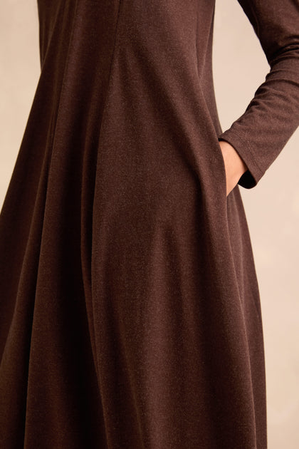 A person wears the Soft Viscose Jersey Bubble Dress with long sleeves in chocolate, one hand resting in the side pocket against a neutral background.