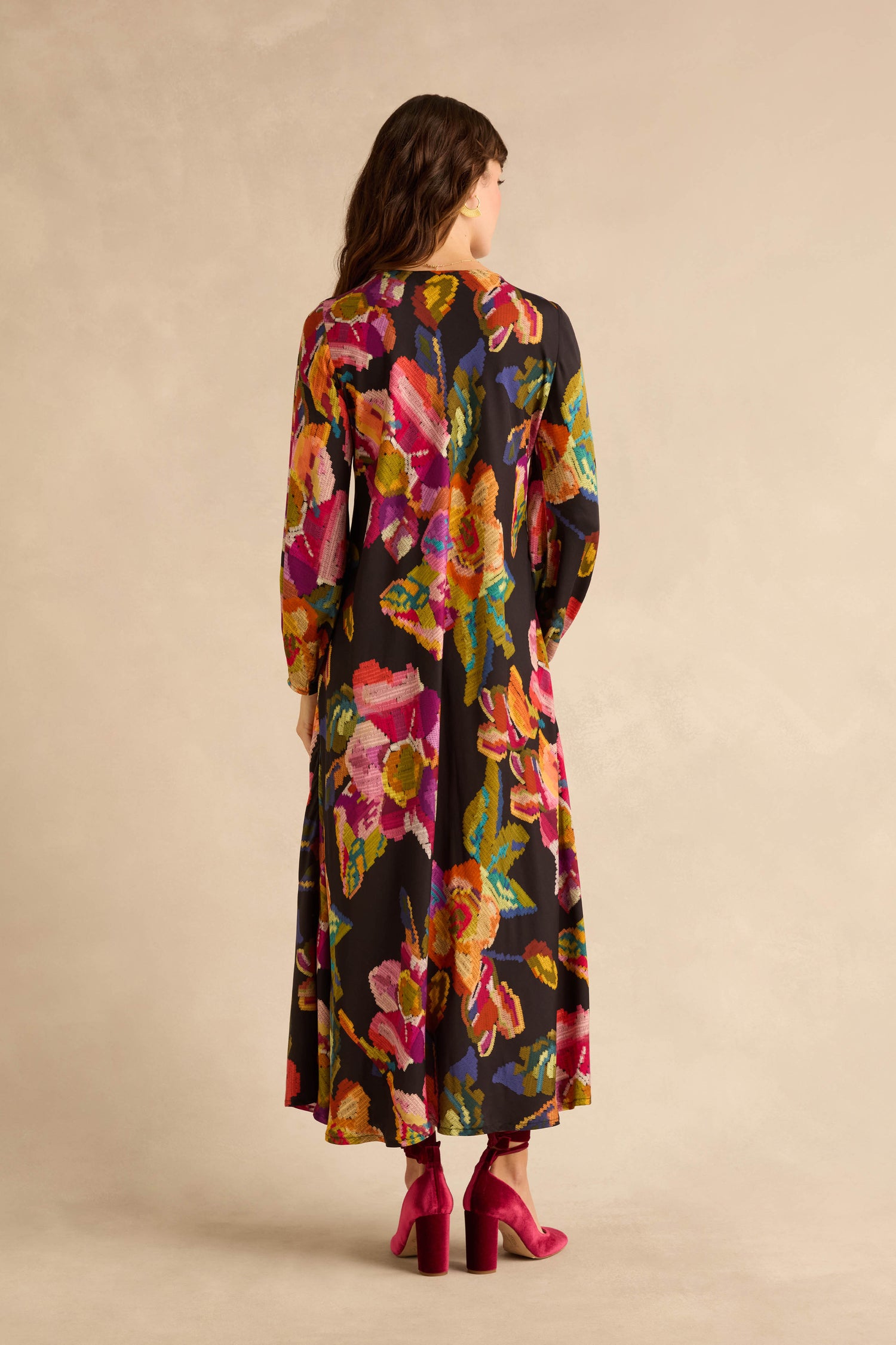 A woman viewed from behind wears a long-sleeved, ankle-length Pixelated Floral Flared Dress and velvet block-heel pumps.