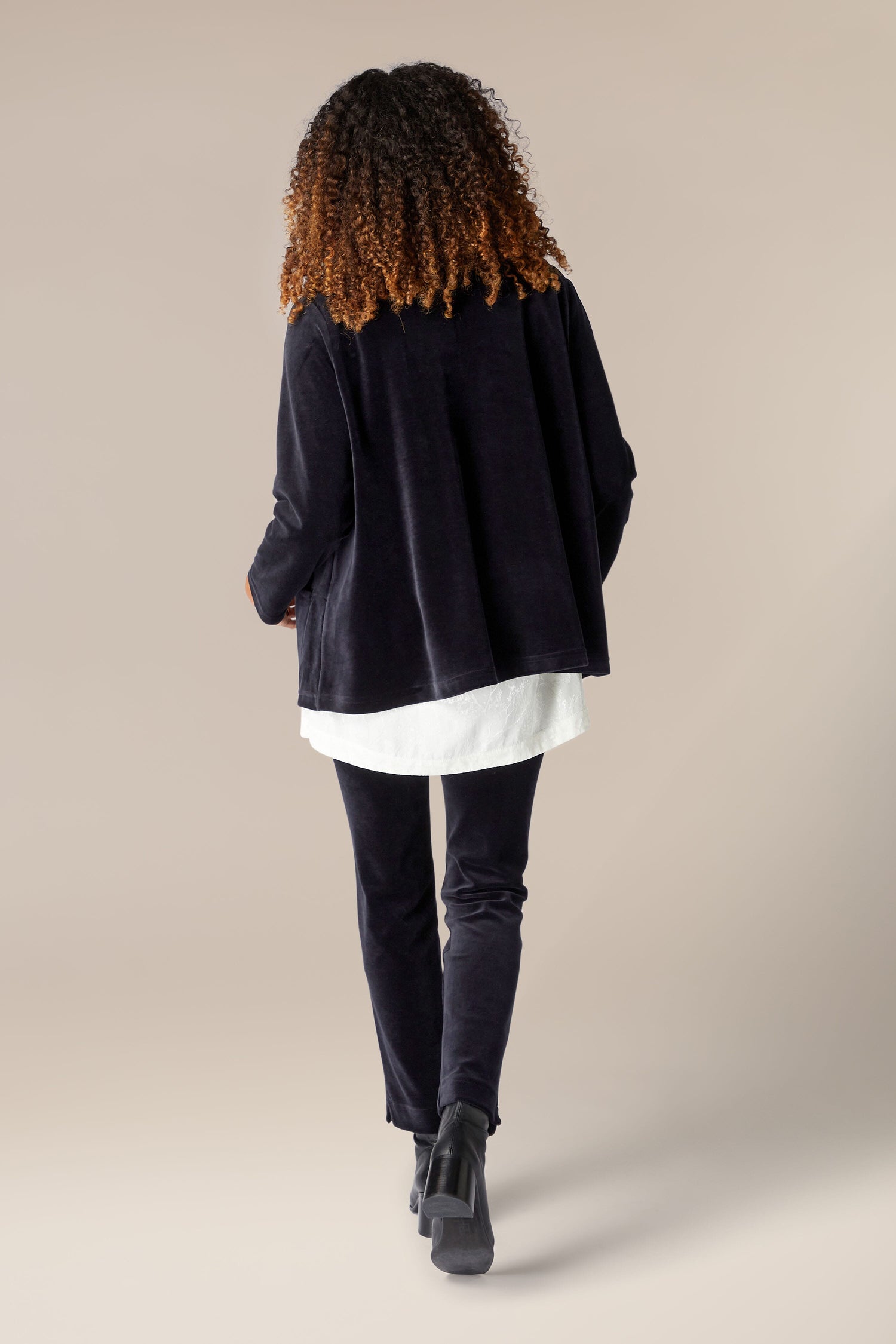 The back view of a woman wearing a luxurious Velvet Jersey Relaxed Jacket and white pants.