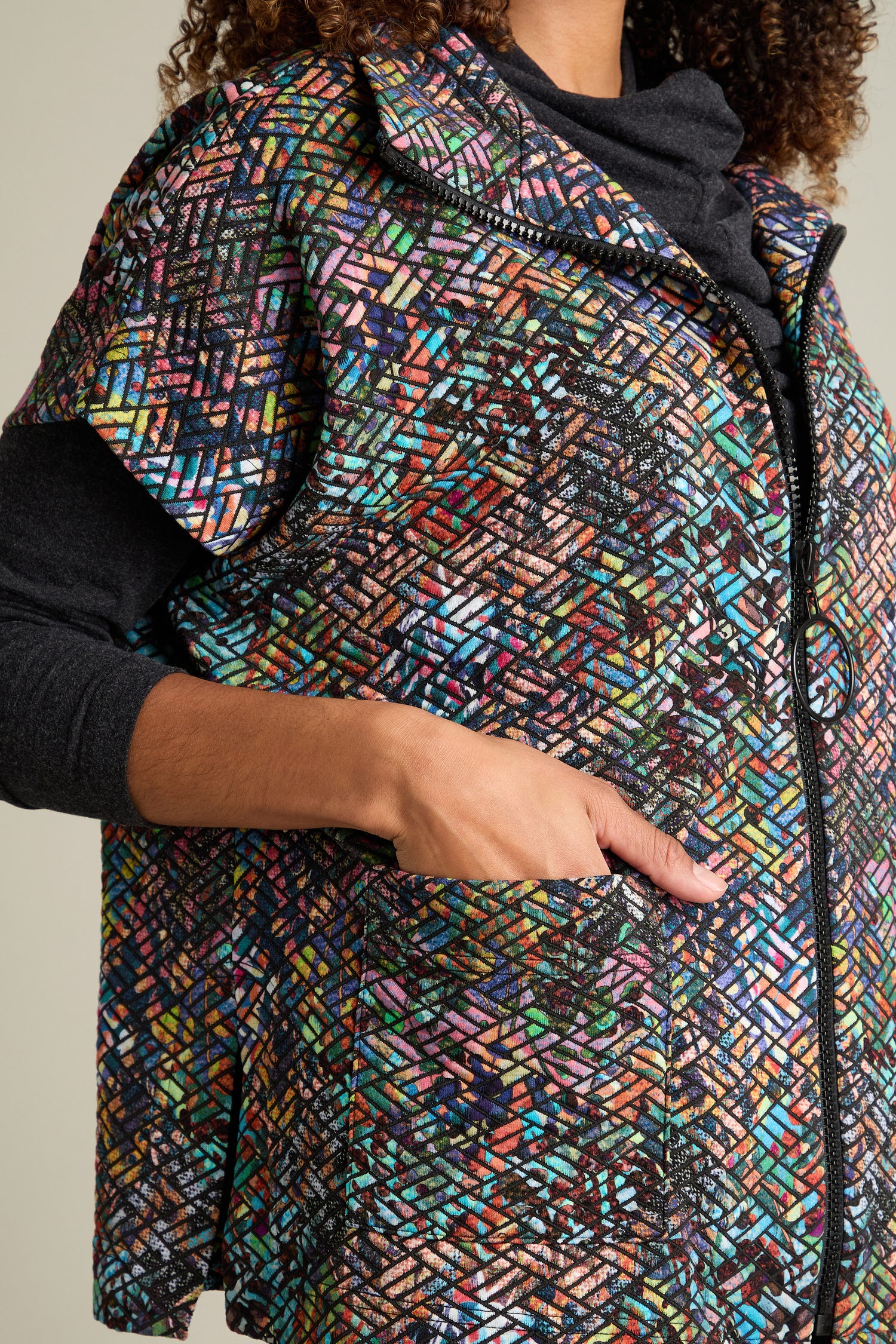 Close-up of a person wearing the Diamond Jacquard Jersey Jacket, featuring a multicolored pattern and a zipper, making it an ideal addition to your seasonal wardrobe. One hand is placed in a pocket against a neutral background.