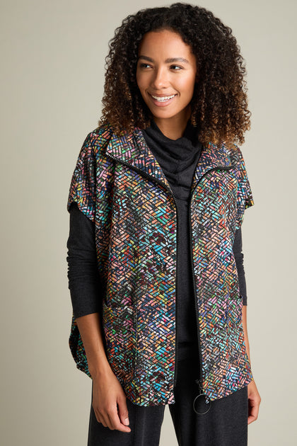 A person with curly hair is smiling and looking slightly to the side against a plain background. They are wearing a black top underneath a Diamond Jacquard Jersey Jacket featuring a vibrant, multi-colored diamond pattern.