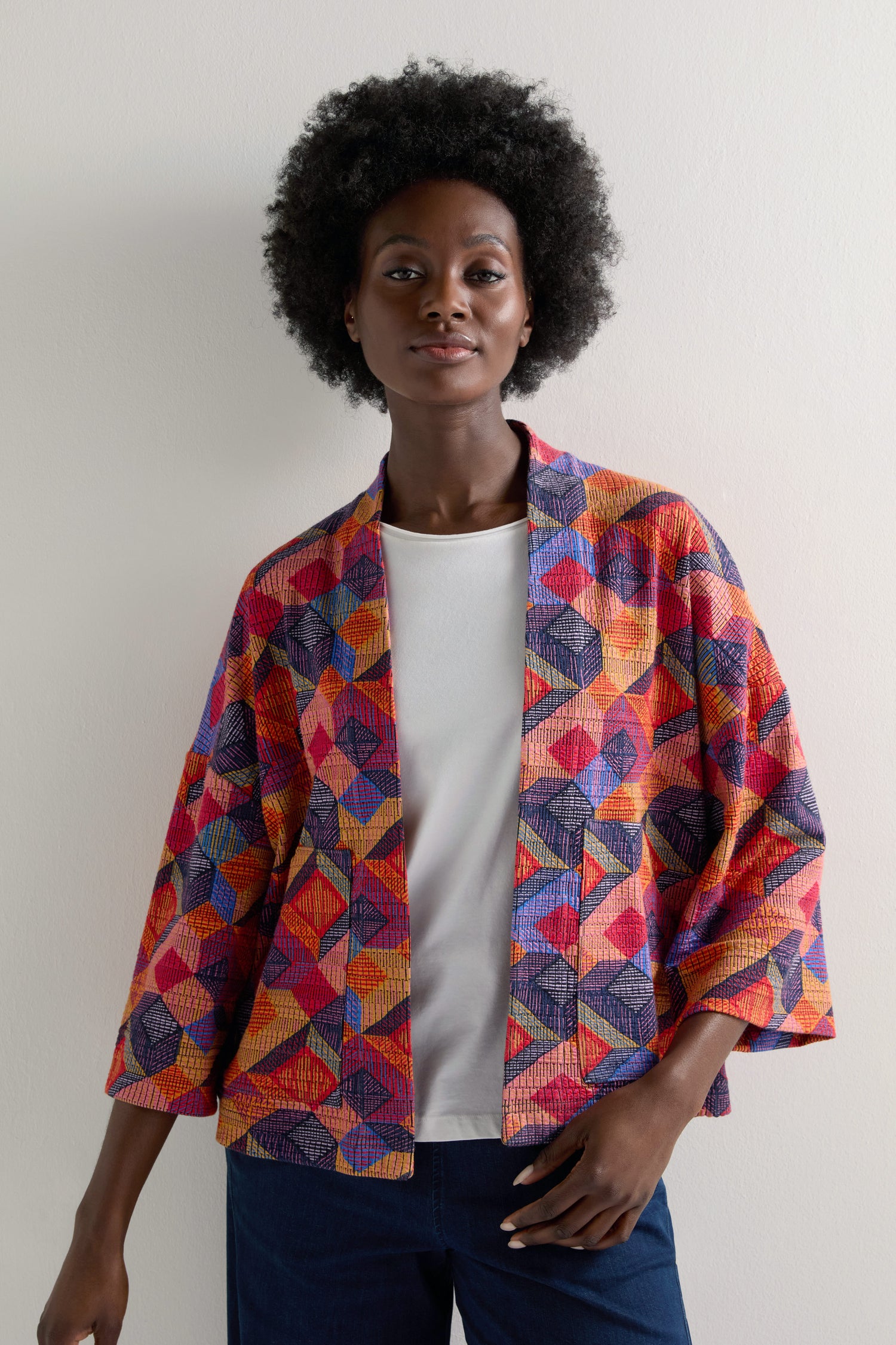 Against a plain backdrop, a person sports the Bold Cubist Print Jacket over a white shirt. The jacket's vibrant geometric patterns lend the ensemble a striking, modern look.