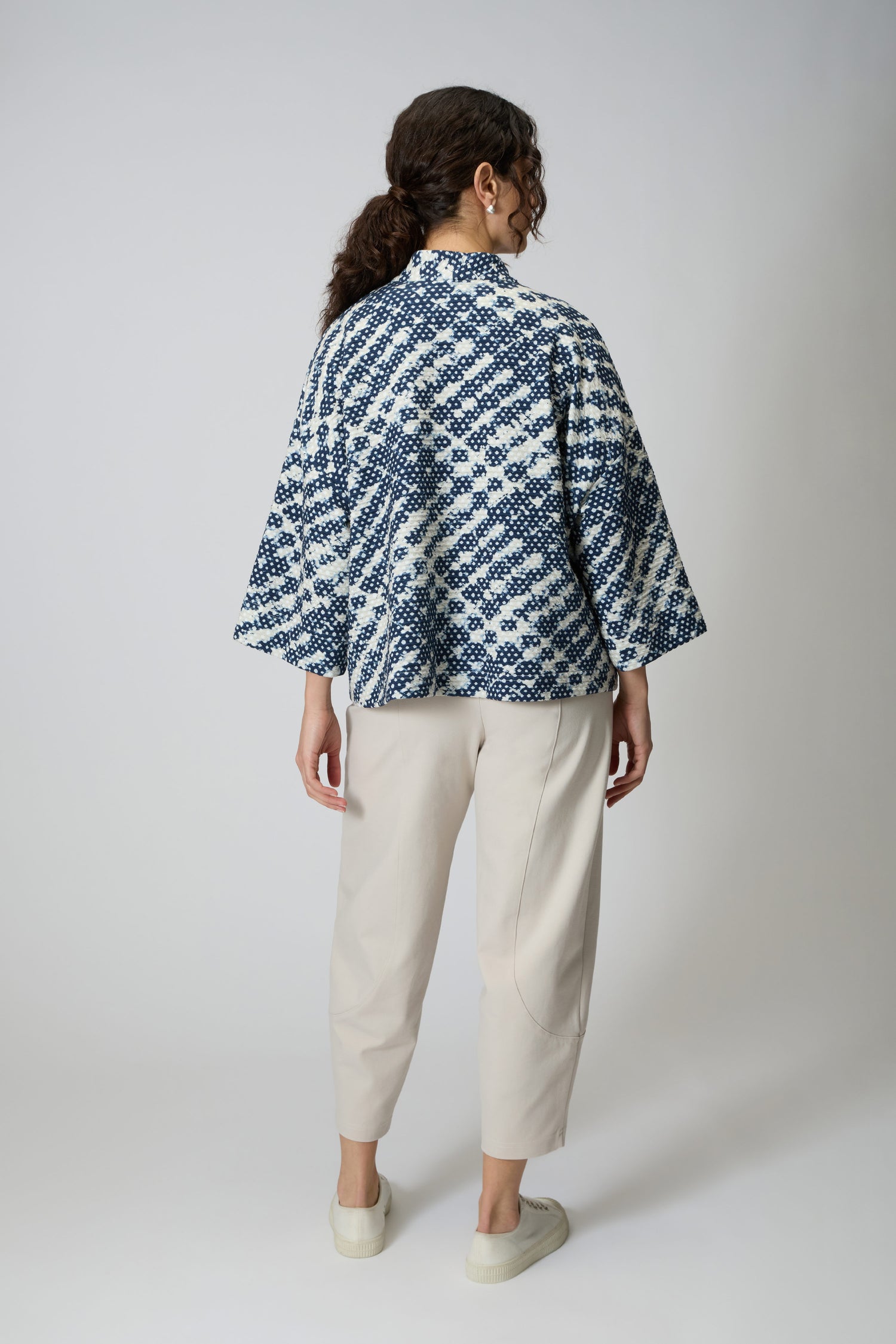 A person stands facing away, wearing the oversized Diamond Tie Dye Jersey Jacket in blue and white, paired with light beige pants and white slip-on shoes against a plain background.