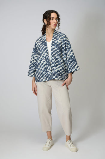 A person wears the Diamond Tie Dye Jersey Jacket in blue and white over a white top, paired with cream cropped pants and white sneakers, standing against a plain light background.