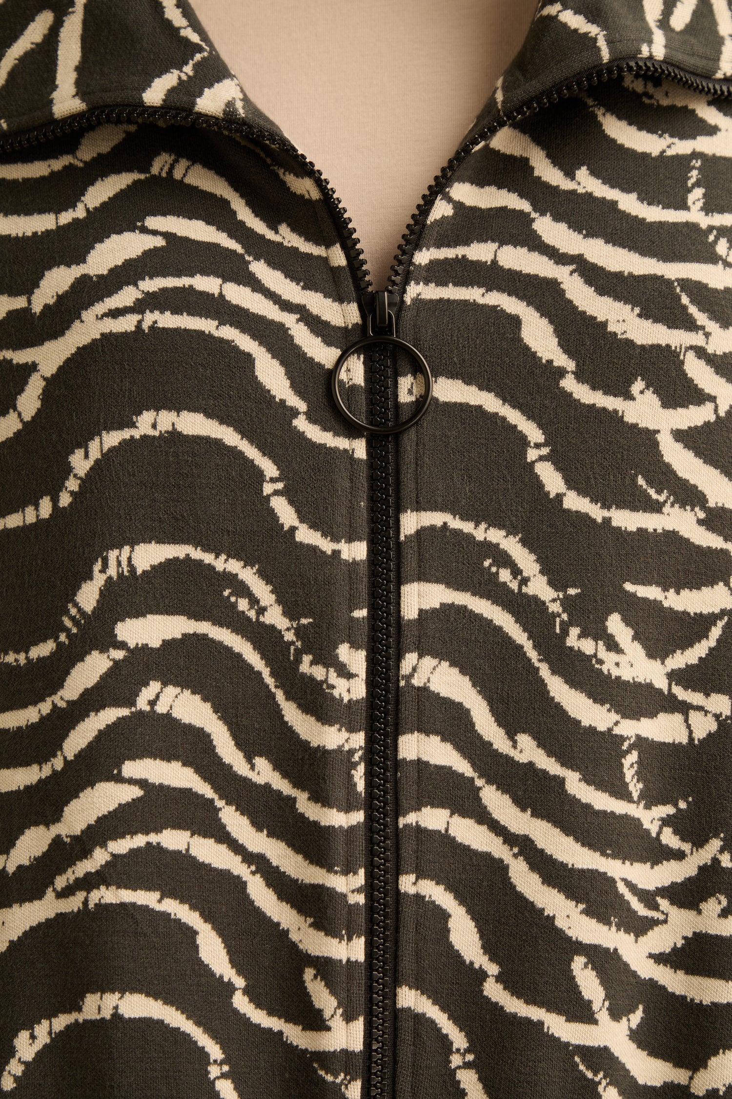 Close-up of the Dancing Waves Zip Boxy Jacket—a black and white stretch jersey zip-up featuring wavy, zebra-like stripes and a boxy silhouette. The jacket is finished with a circular pull tab on the zipper.