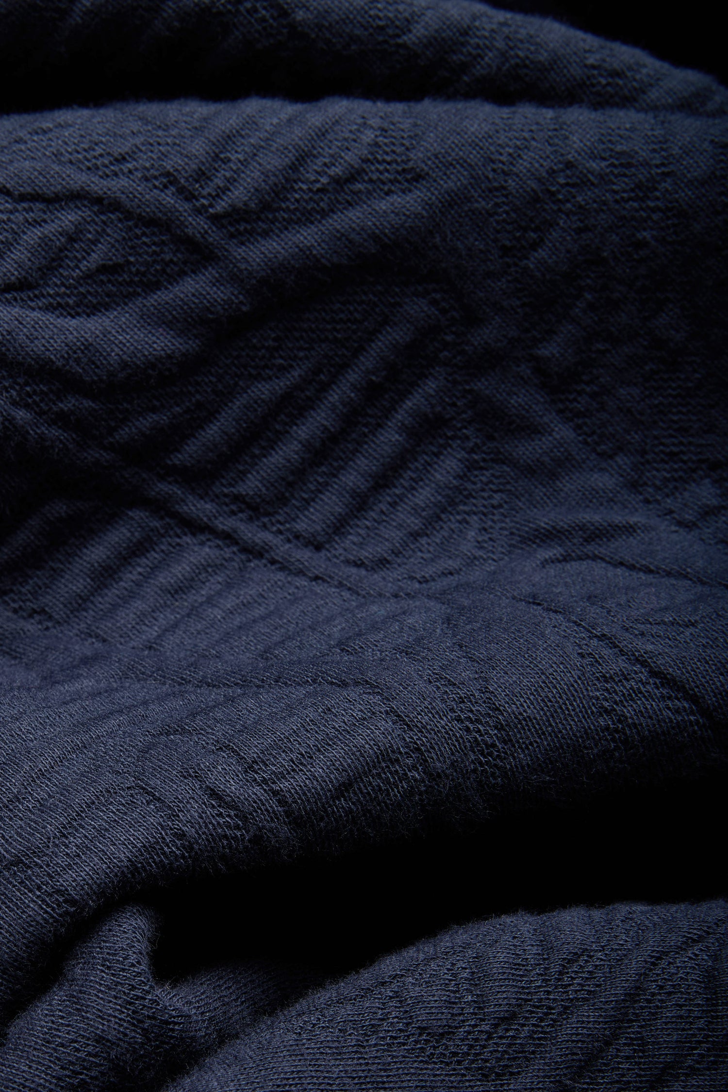 Close-up of dark navy blue textured fabric from the Quilted Zip Through Jacket, featuring visible stitching and subtle diagonal quilted patterns.