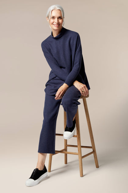 A woman sitting on a stool in Marl Jersey Wide Leg Trousers and a blue sweater.