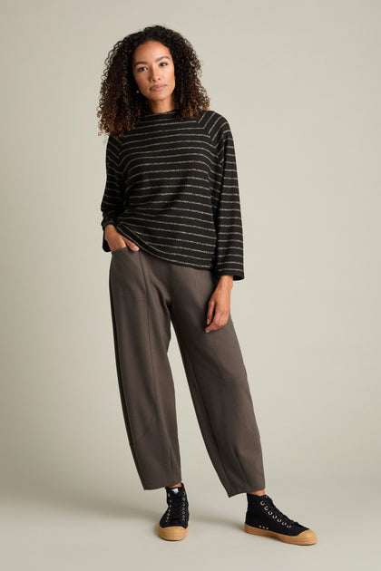 A person stands against a plain background, flaunting their contemporary style in a striped sweater paired with Marl Jersey Bubble Trousers and black sneakers with brown soles.