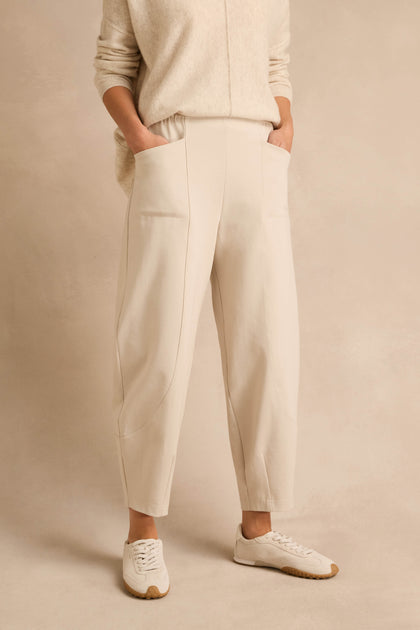 Wearing the Ecru Ponte Bubble Trousers, a matching sweater, and white sneakers, a person stands with hands in pockets against a neutral background.