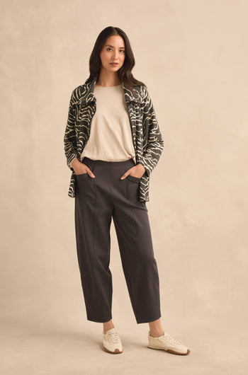 Woman standing with hands in pockets, wearing a patterned jacket, white shirt, Slate Ponte Bubble Trousers with an elasticated waist, and white sneakers against a beige background.