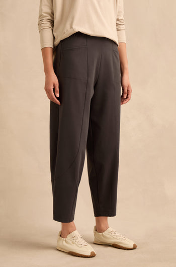 A person is standing against a plain beige background wearing a beige long-sleeve top, the Slate Ponte Bubble Trousers with an elasticated waist, and white sneakers.