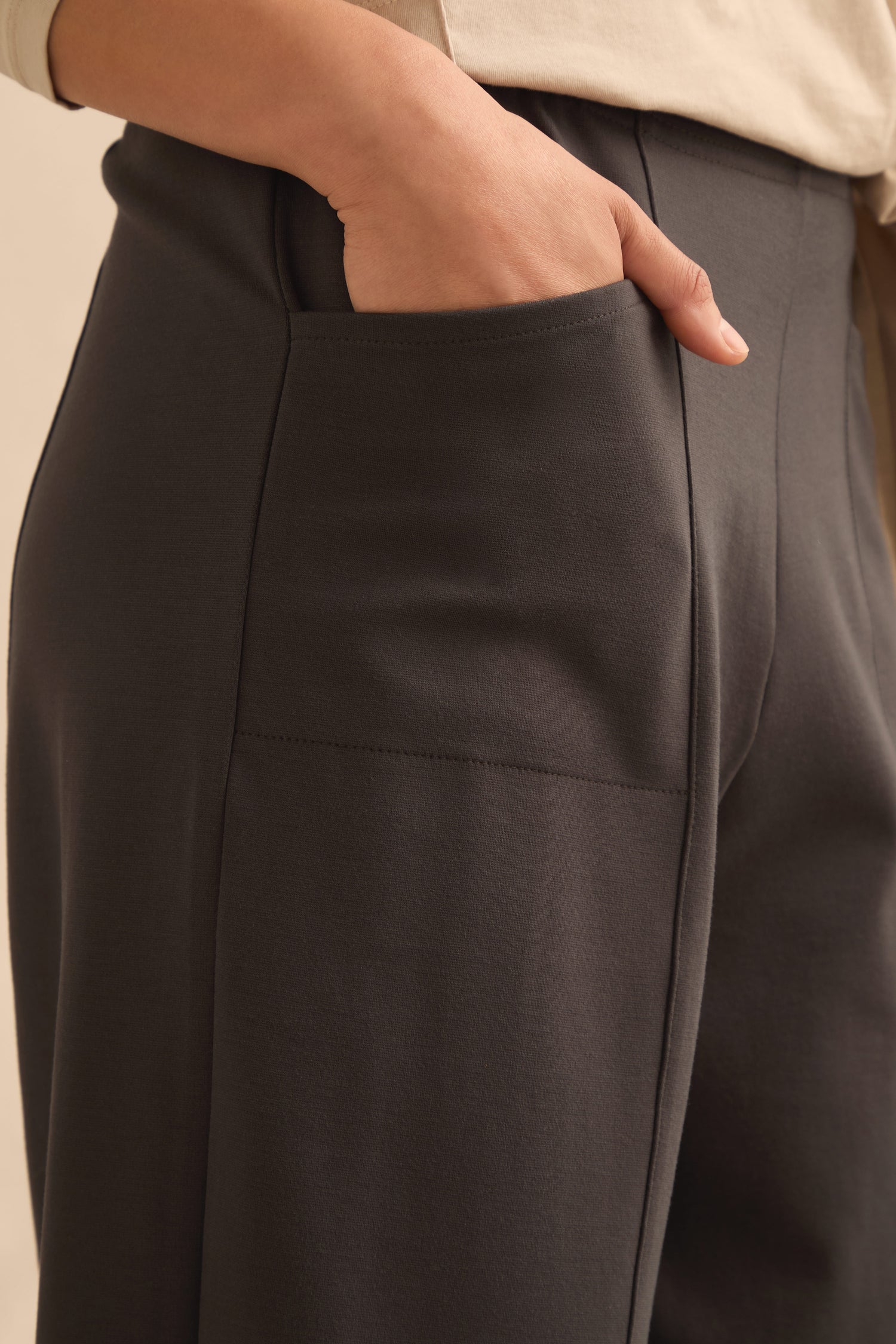 Wearing the Slate Ponte Bubble Trousers featuring an elasticated waist, the person places their right hand in the pocket, highlighting a close-up of the side seam and pocket detailing.
