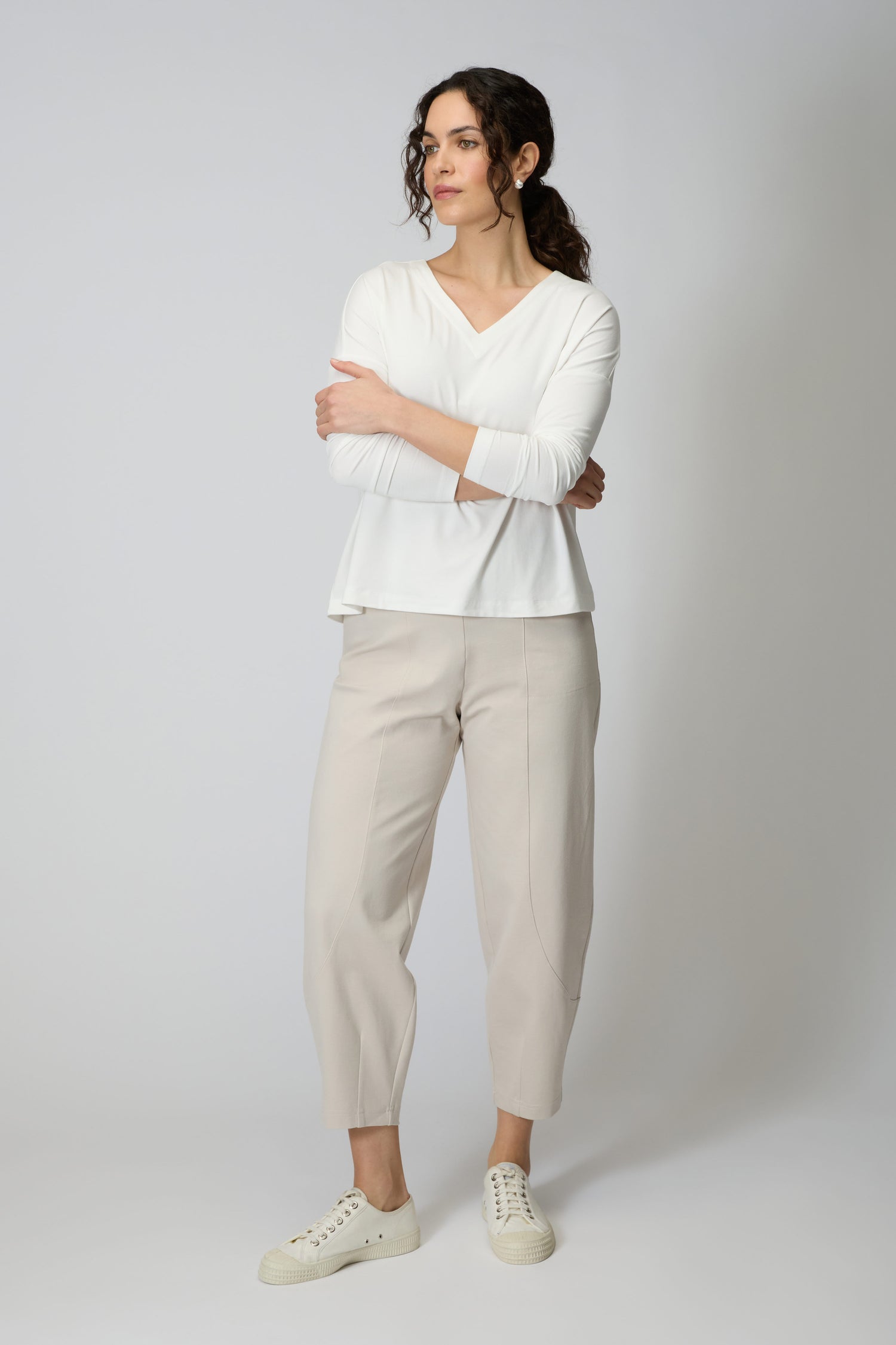 A woman stands with arms crossed, wearing a white long-sleeve top, Ecru Ponte Bubble Trouser with a bubble leg silhouette, and white sneakers against a plain light background.