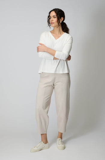 A woman stands with arms crossed, wearing a white long-sleeve top, Ecru Ponte Bubble Trouser with a bubble leg silhouette, and white sneakers against a plain light background.