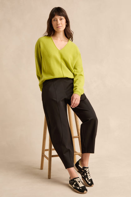 Woman wearing a lime green sweater, Black Ponte Bubble Trousers, and black sneakers sits on a wooden stool against a neutral background.