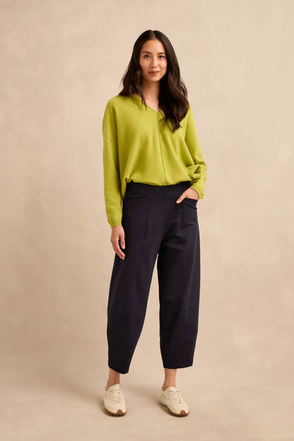 A woman stands facing forward wearing a lime green sweater, the Midnight Ponte Bubble Trousers in a dark rounded leg silhouette, and white sneakers against a neutral beige background.