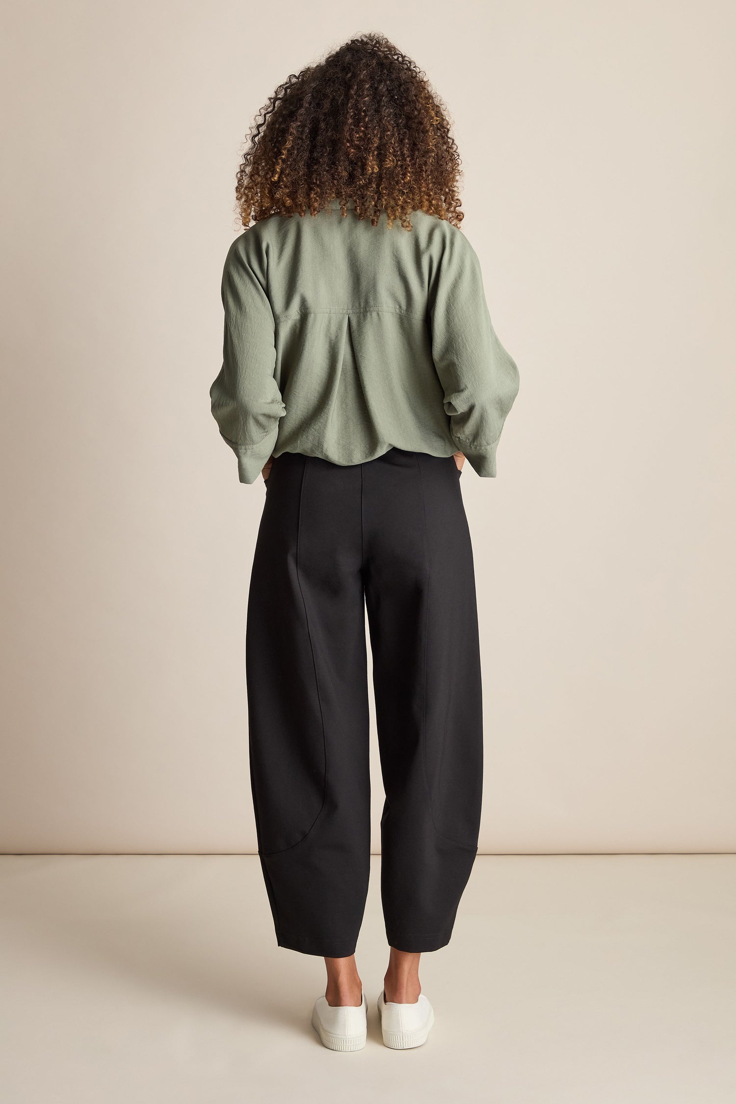 A person with curly hair, wearing a green top, white shoes, and the Ponte Bubble Trouser featuring an elasticated waistband in black, is standing facing away from the camera against a plain background.