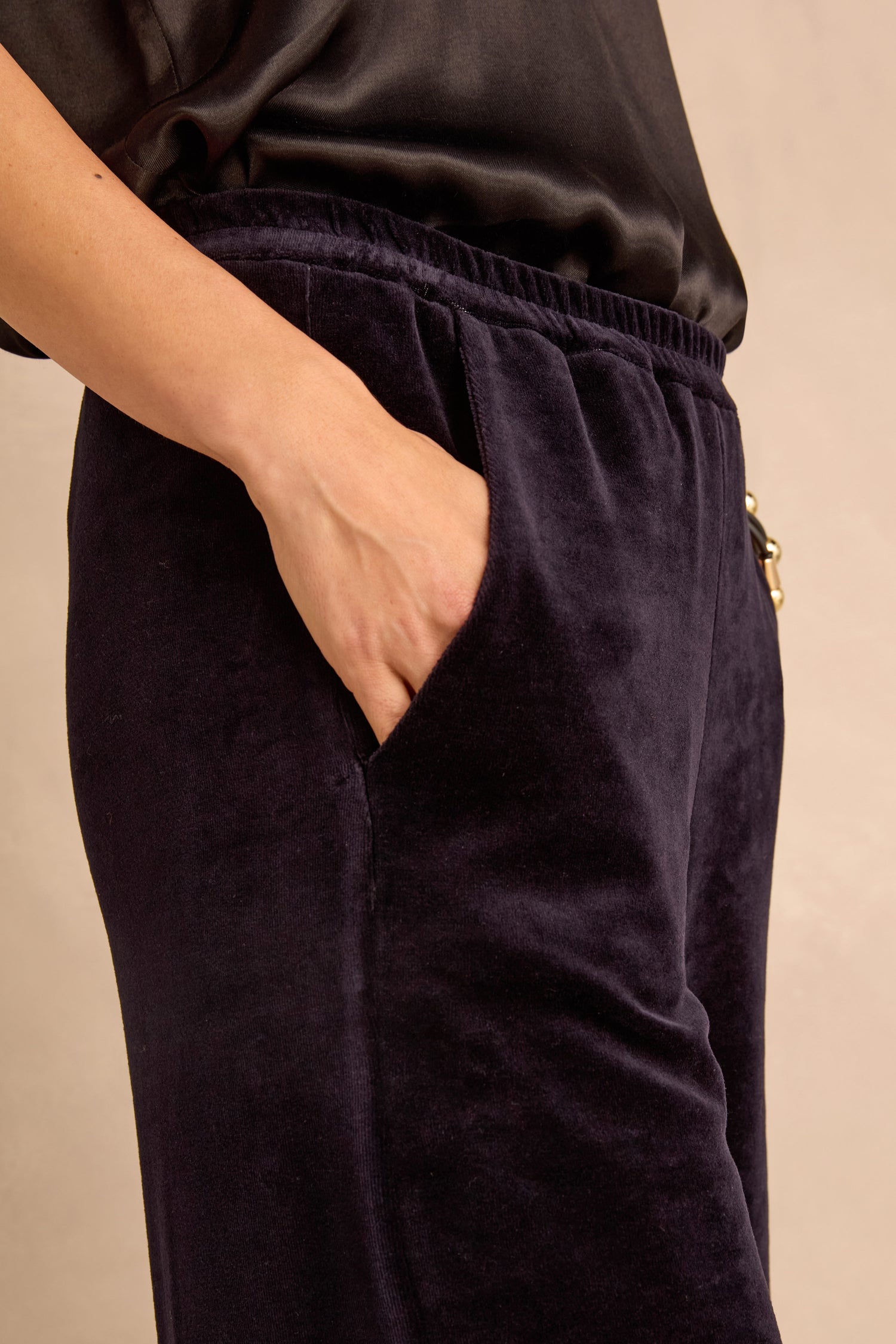 A person wearing the Night Velvet Jersey Bubble Trousers and a black satin top stands with one hand in their pocket against a neutral background, showcasing the trousers’ subtle bubble silhouette.