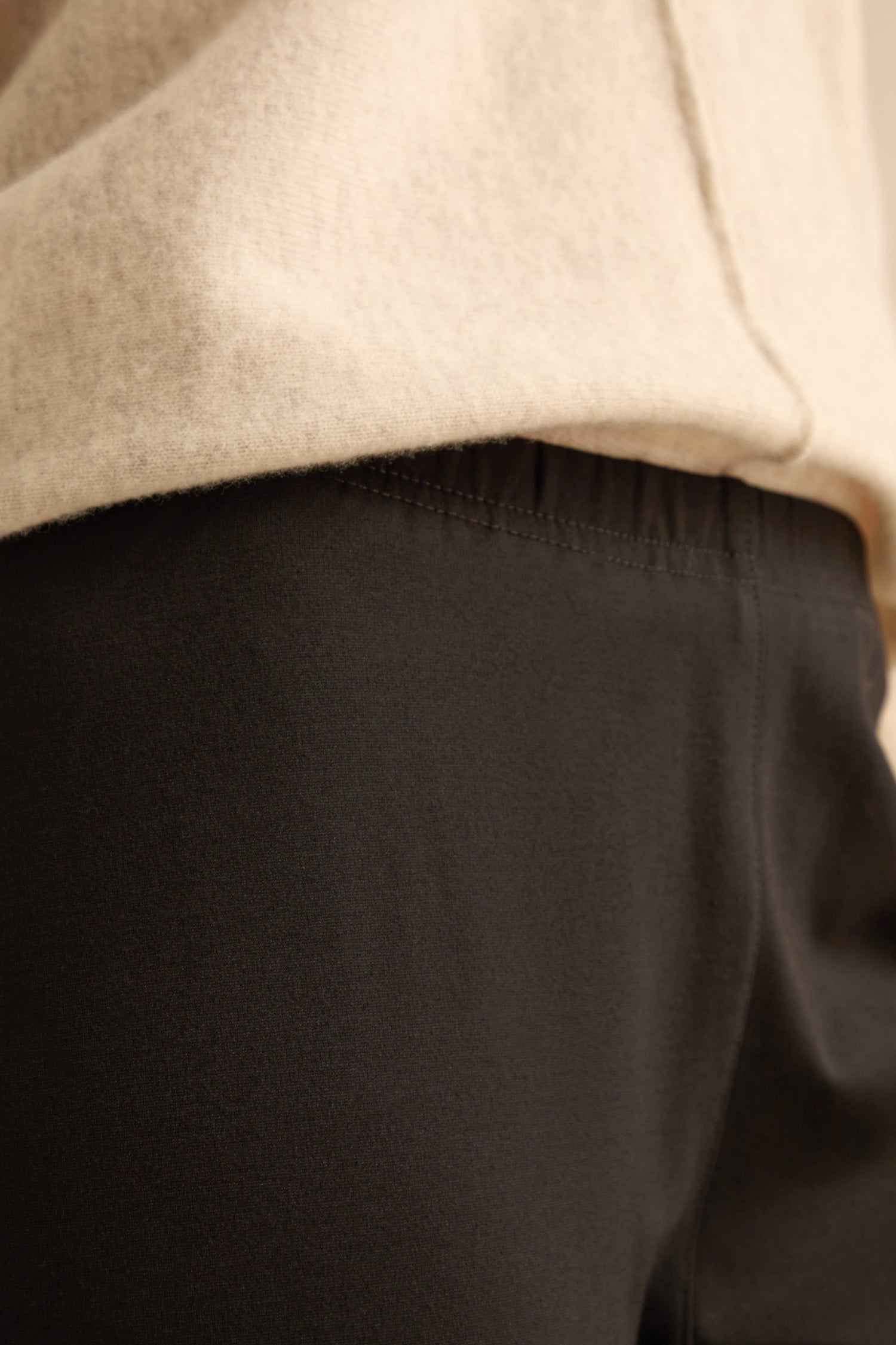 Close-up of a person wearing a beige sweater and Black Ponte Slim Leg Trouser, focusing on the waist area where the two pieces of clothing meet.
