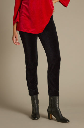 A person wearing a red top and Velvet Jersey Slim Leg Trousers stands with one hand on their hip. They are also sporting black ankle boots.