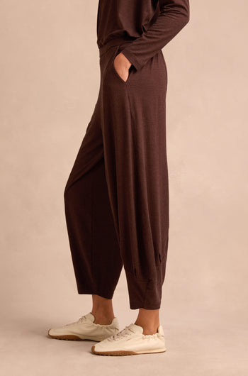 Wearing the Soft Viscose Jersey Bubble Trouser—loose brown trousers with a relaxed fit and pockets—paired with a matching long-sleeve top and white sneakers, this person stands against a neutral background.