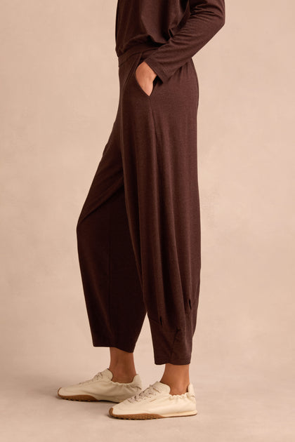 Wearing the Soft Viscose Jersey Bubble Trouser—loose brown trousers with a relaxed fit and pockets—paired with a matching long-sleeve top and white sneakers, this person stands against a neutral background.