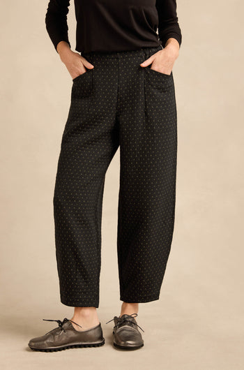 A person wearing a black long-sleeve top and the Square Jacquard Bubble Trousers—with a cotton-rich blend featuring subtle polka dots—paired with metallic oxford shoes, stands with hands in pockets against a neutral background.