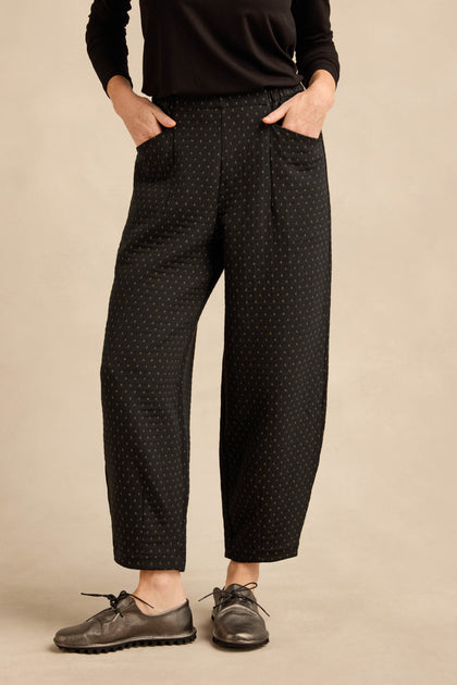 A person wearing a black long-sleeve top and the Square Jacquard Bubble Trousers—with a cotton-rich blend featuring subtle polka dots—paired with metallic oxford shoes, stands with hands in pockets against a neutral background.