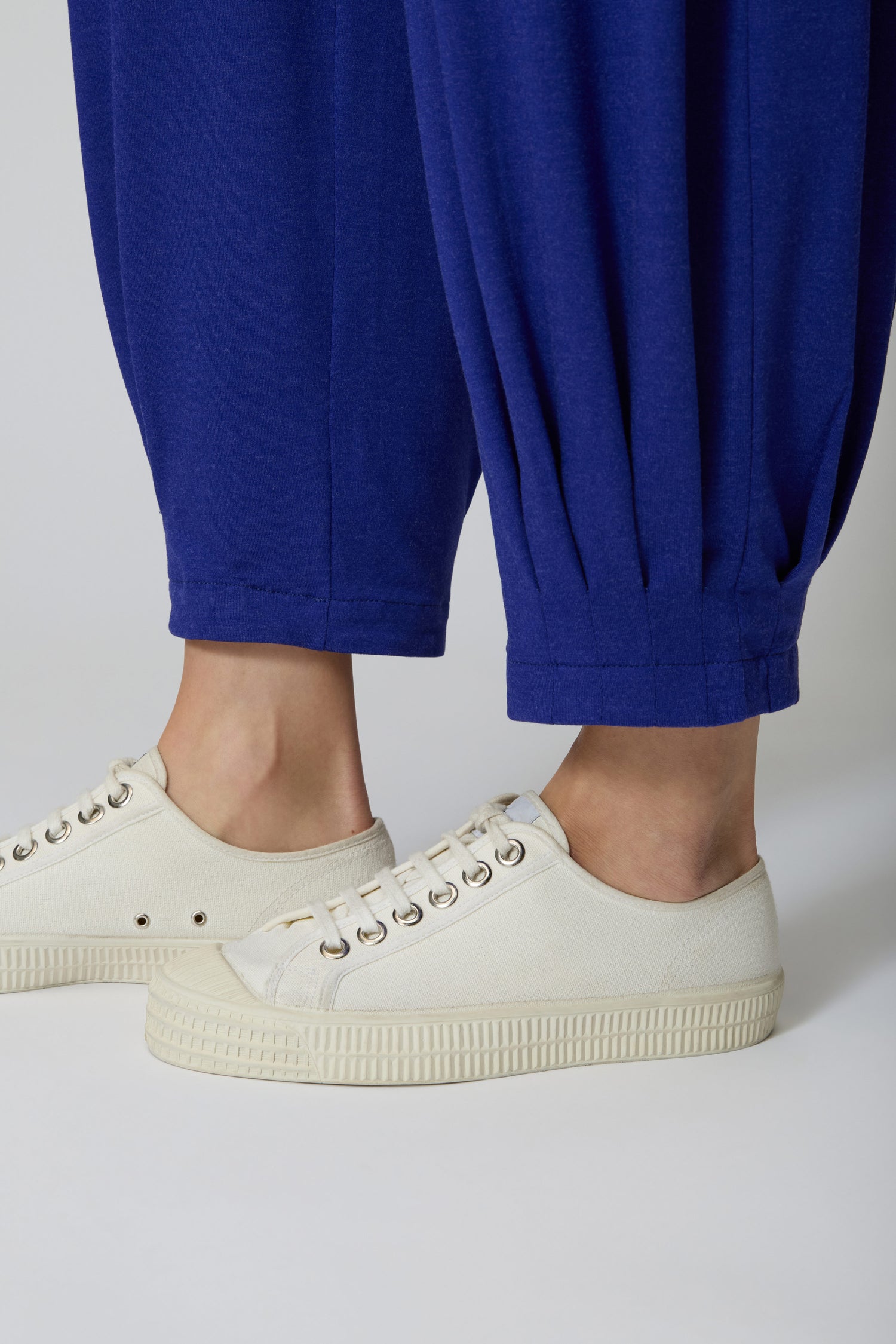 Someone in Soft Viscose Jersey Bubble Trousers in bright blue and off-white canvas sneakers stands on a light-colored surface.