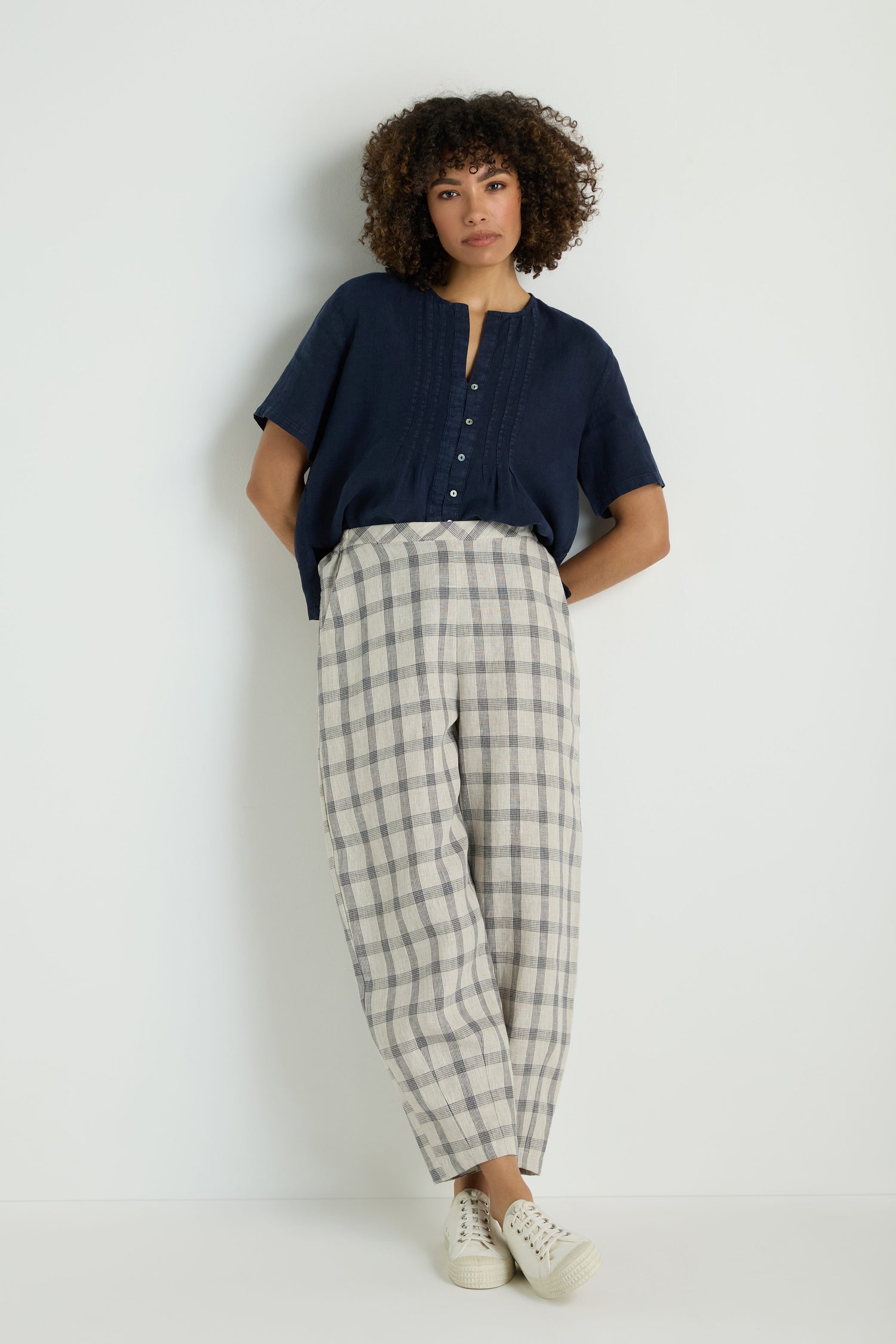 Person wears Grid Check Linen Bubble Trouser, styled high-waisted and loose with hands in pockets, light top, and brown woven slip-on shoes against a plain background.