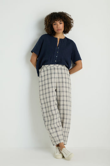Person wears Grid Check Linen Bubble Trouser, styled high-waisted and loose with hands in pockets, light top, and brown woven slip-on shoes against a plain background.