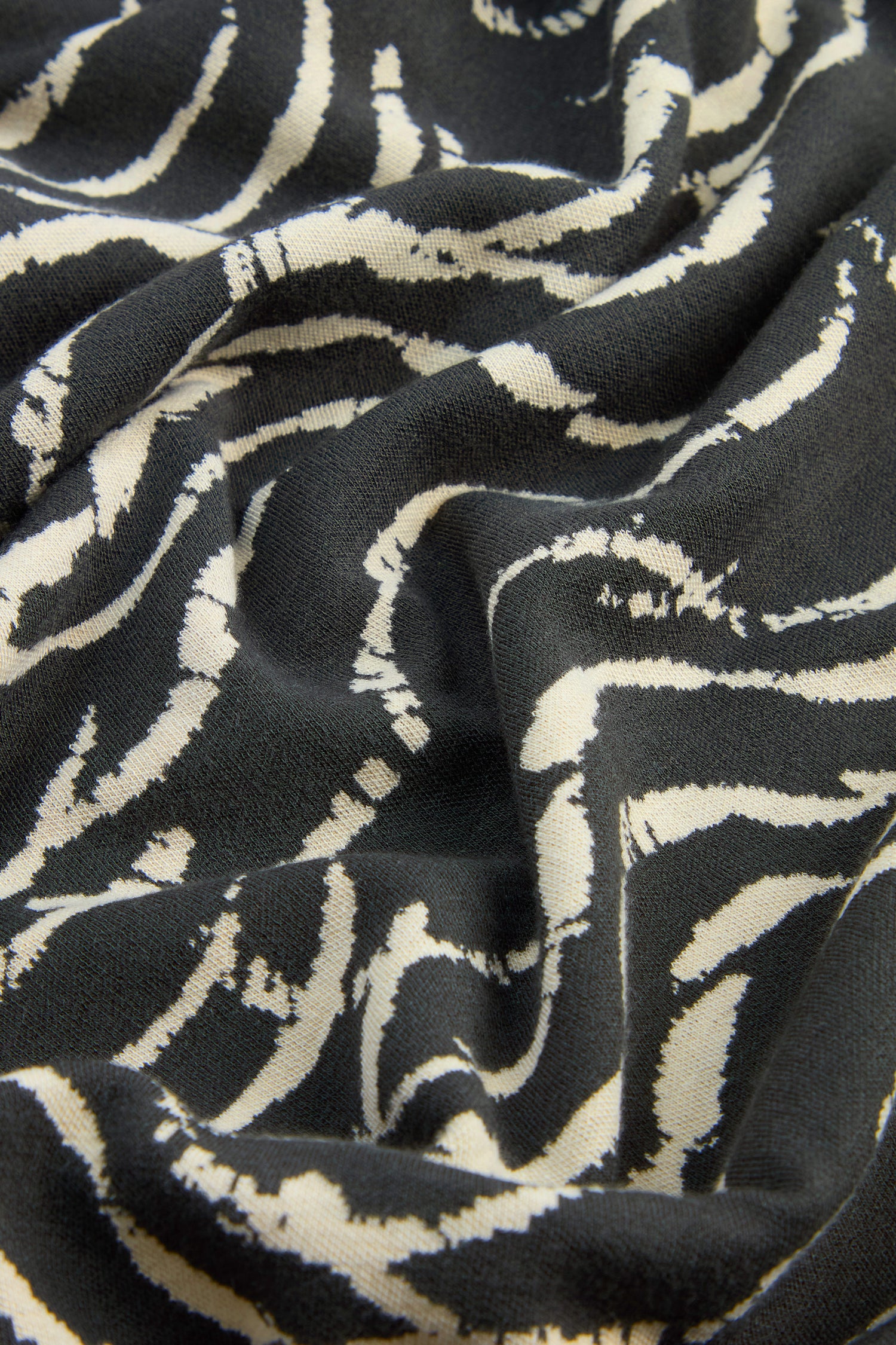 Close-up of black fabric with white wavy, irregular striped patterns reminiscent of the Dancing Waves design and a slightly wrinkled texture, crafted in stretch jacquard that’s ideal for the Dancing Waves Jersey Bubble Trousers.